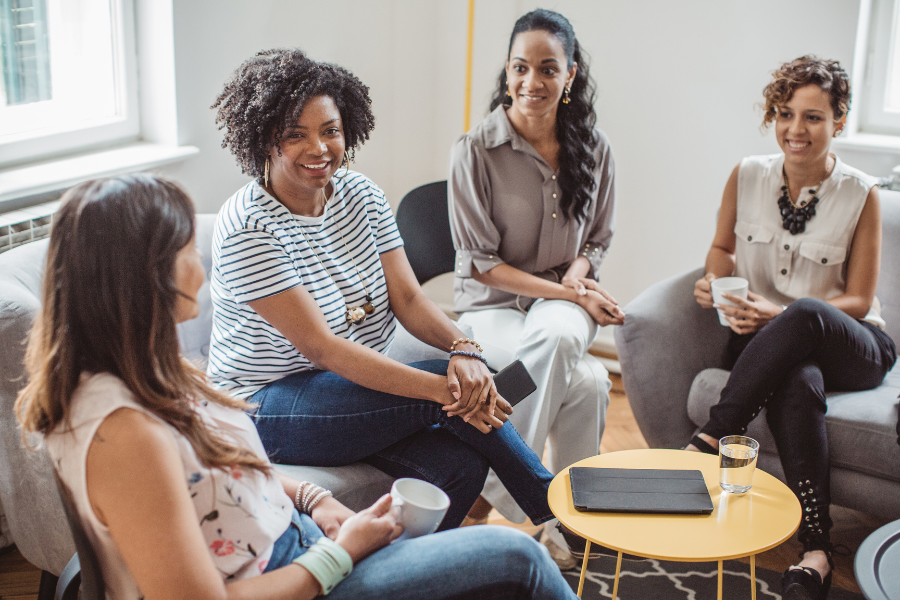 Women sitting in a support circle drinking coffee and smiling | Programs