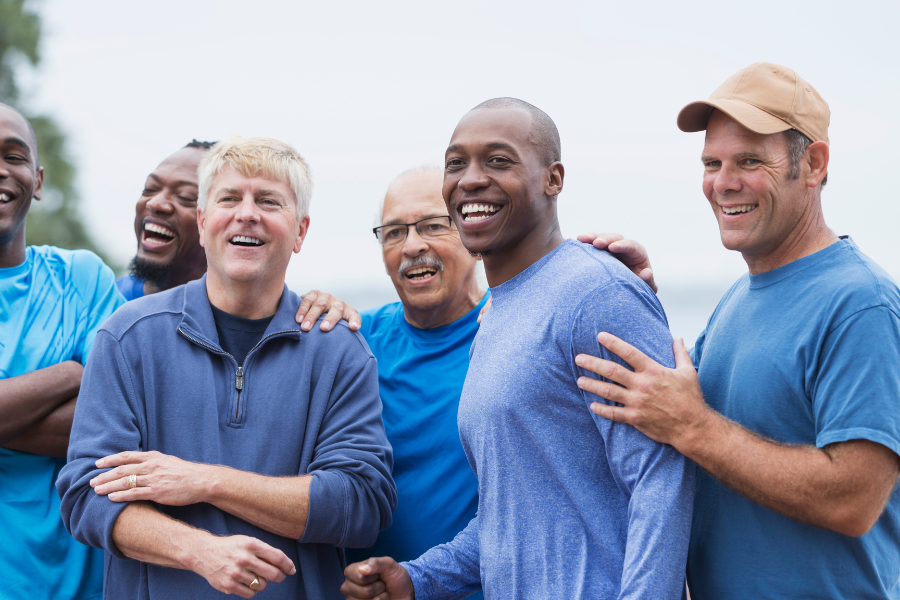 Group of older men smiling and gathered outdoors in blue shirts