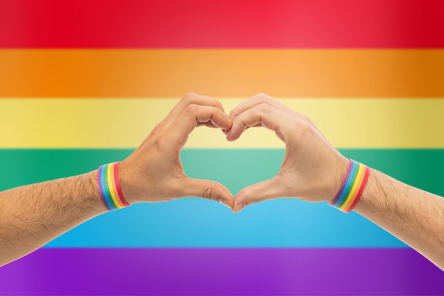 Rainbow flag background with hands forming a heart wearing pride bracelets